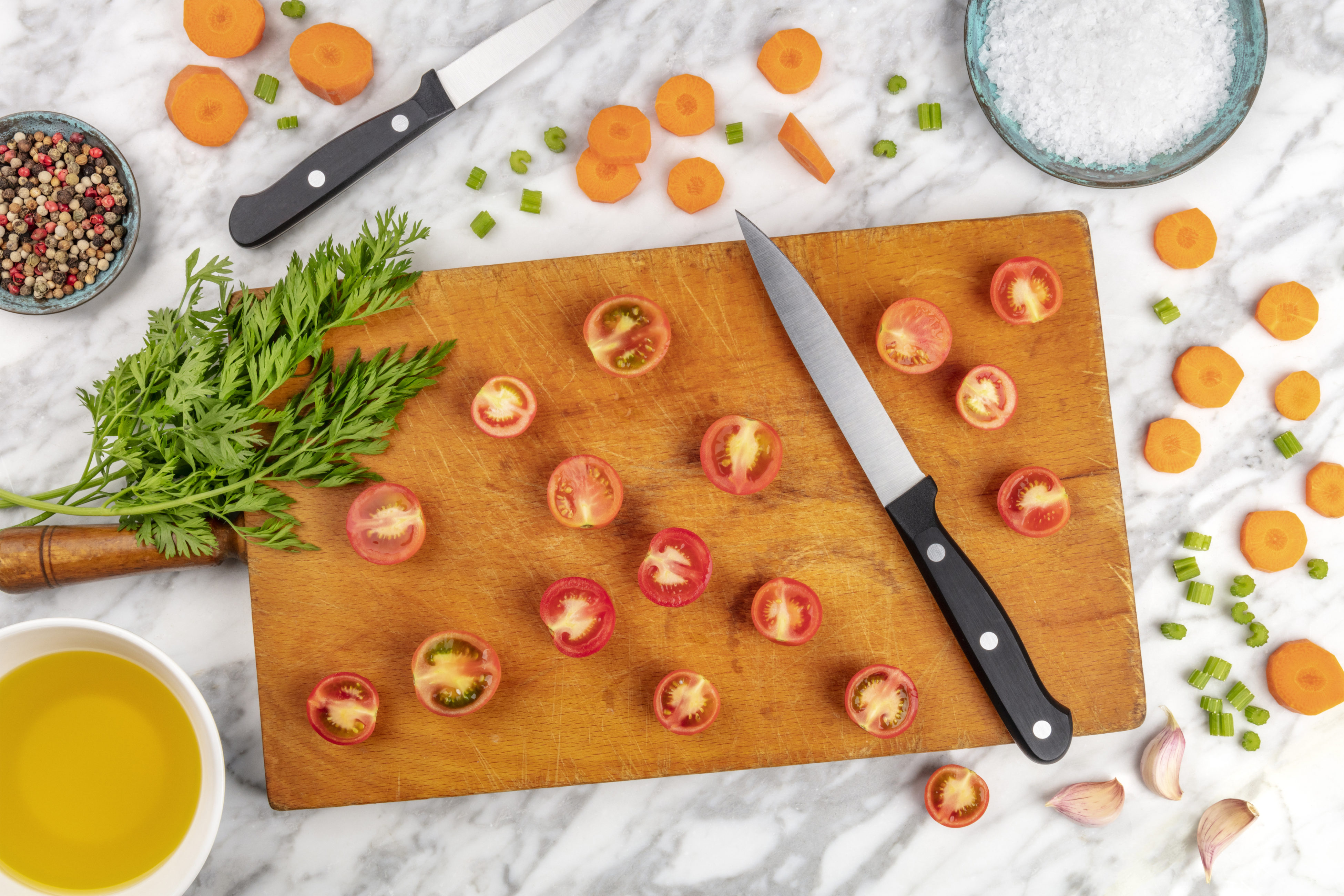 Prep time, or mise en place. An overhead photo of a professional chef's knife, shot from above on a cutting board, with chopped vegetables and spices, on a marble cooking surface