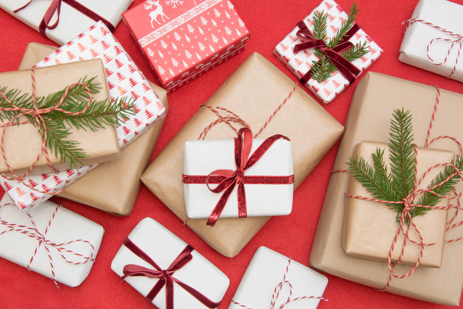 Christmas gift box wrapped in ornament paper and decorative red rope ribbon on red surface. Creative hobby, top view. Prepare to Xmas.