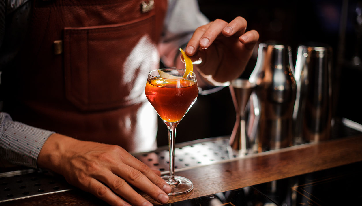 Bartender with glass and lemon peel preparing cocktail at bar