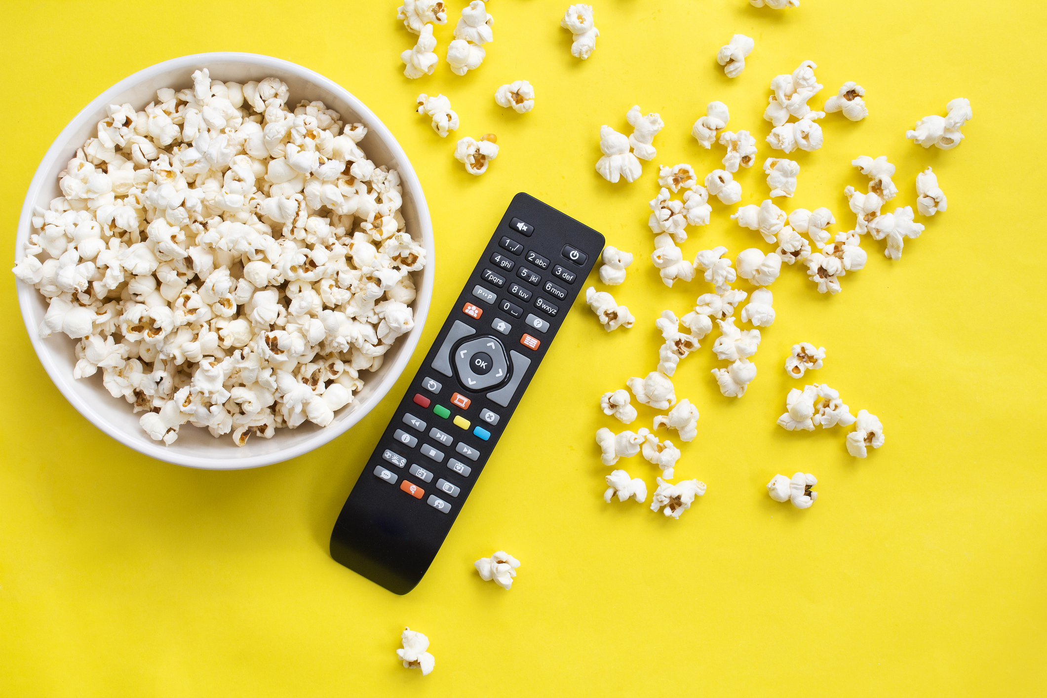 Popcorn and remote control viewed from above on yellow background. Flat lay of pop corn bowl. Top view