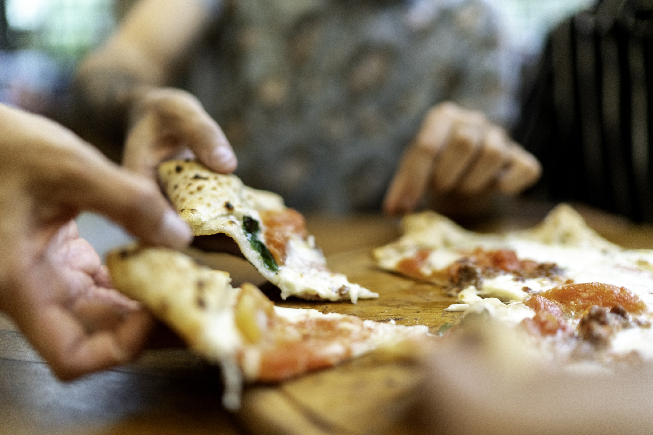 Friends getting slices of pizza, using hands