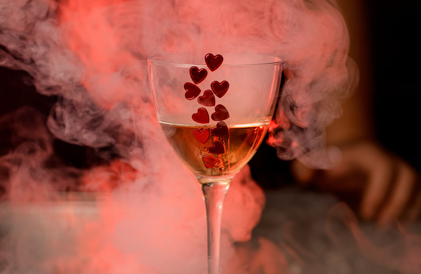 wine glass with drink decorated with red hearts stands on the bar and smoke around