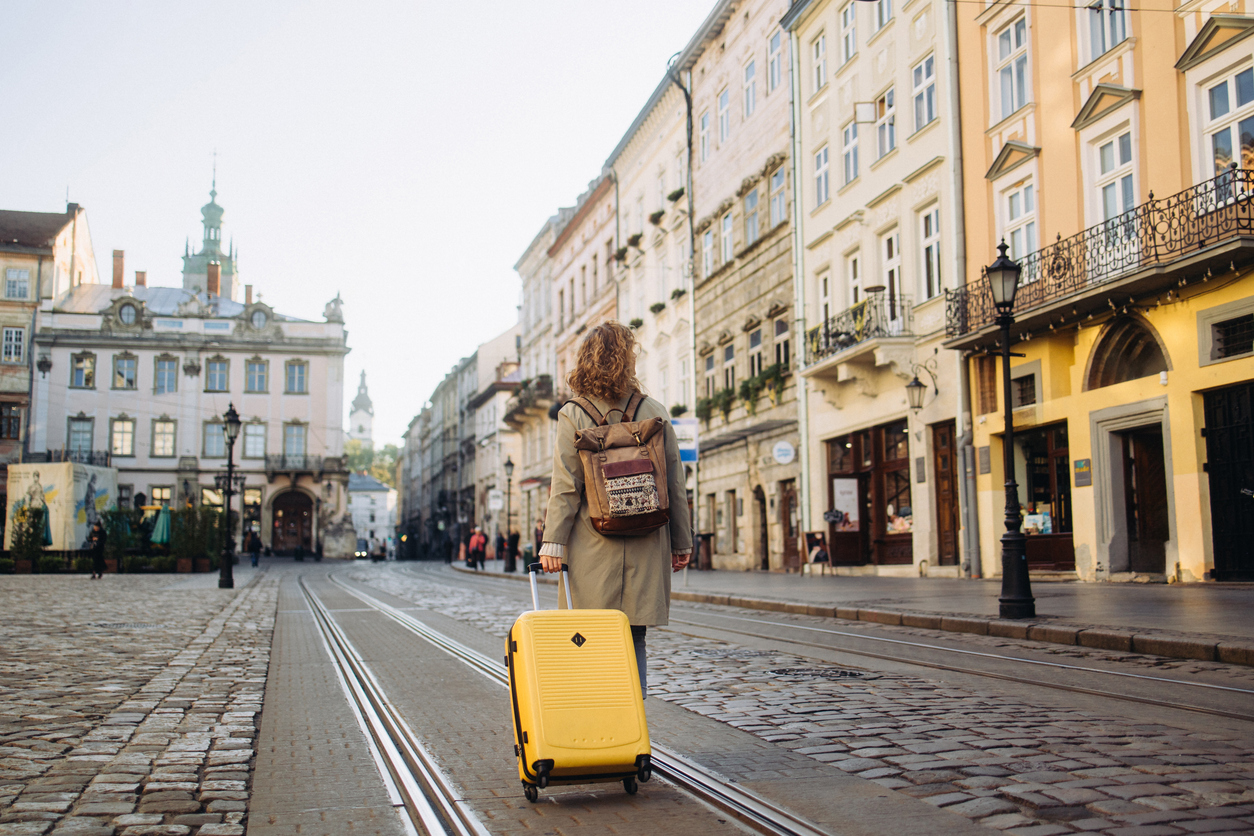 The beautiful cheerful woman with a suitcase walking on an ancient European street in the autumn